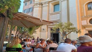 Un café en plein air, avec des tables et des chaises, entouré de bâtiments à l’architecture classique.