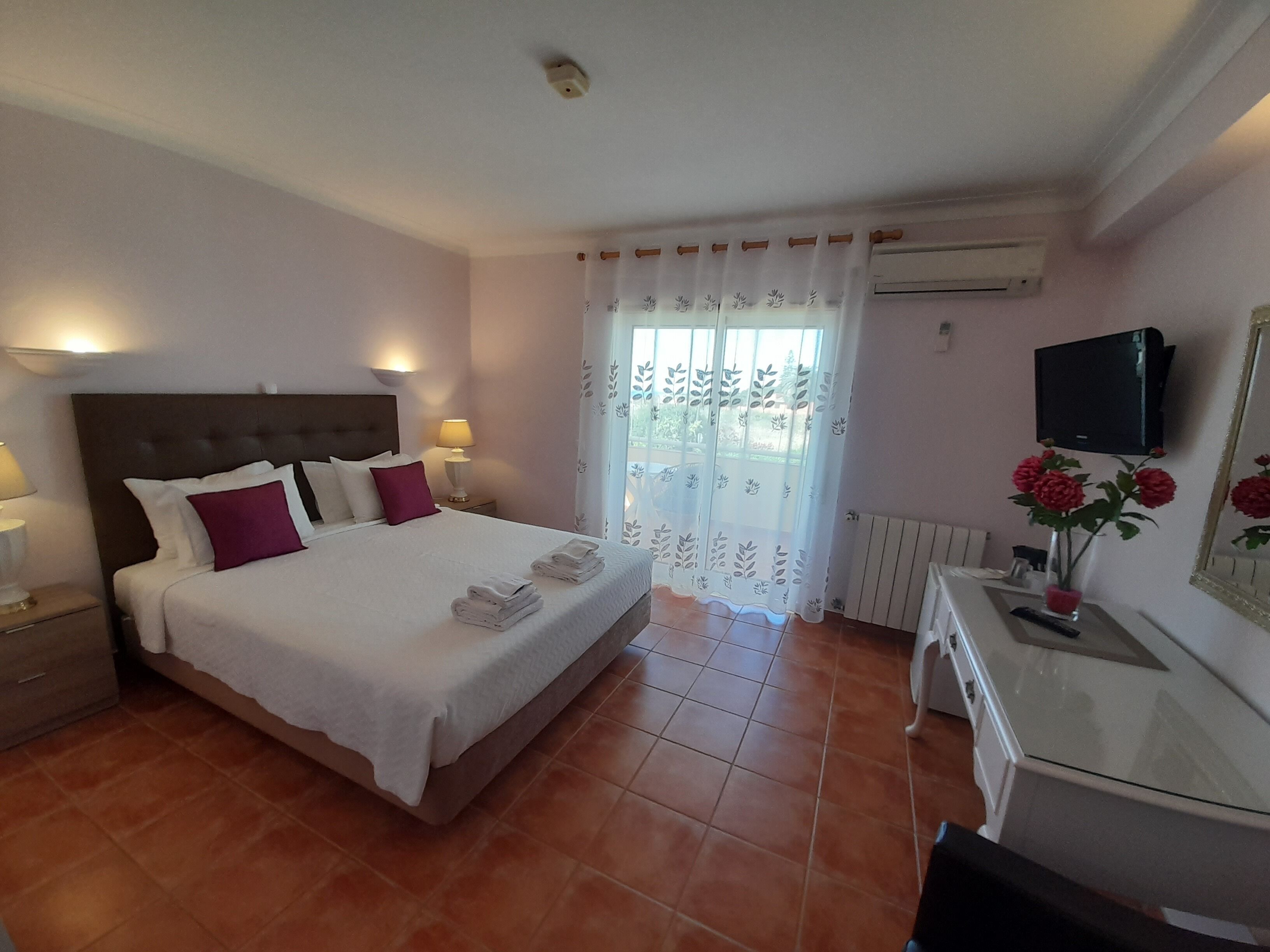 Ein Hotelzimmer mit Bett, Nachttischlampen, einem Schreibtisch mit Fernseher, einem Heizkörper und einem Fenster mit Vorhang.