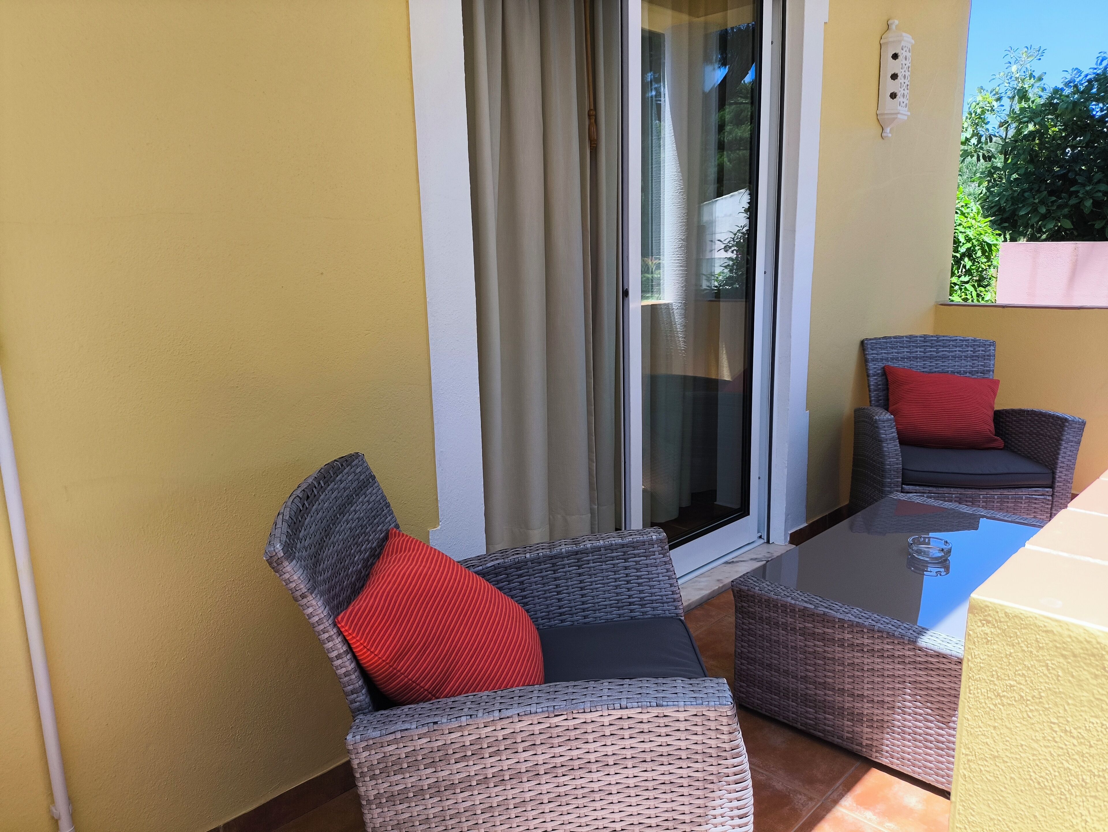 Een balkon met rieten meubels, een glazen tafel en een schuifpui.