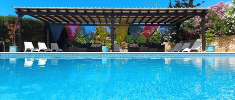 A pool with lounge chairs, a pergola, and potted plants.