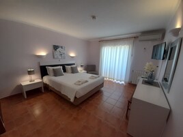 Una habitación de hotel con una cama grande, mesitas de noche, un escritorio y una ventana con cortinas.