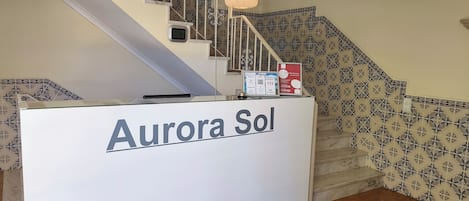 A reception desk labeled 'Aurora Sol' with a staircase in the background.