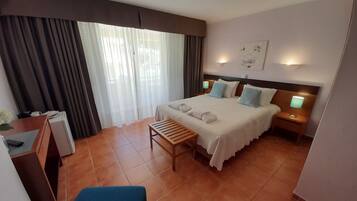 A hotel room with a bed, a desk, a chair, a nightstand, and a wall-mounted lamp.