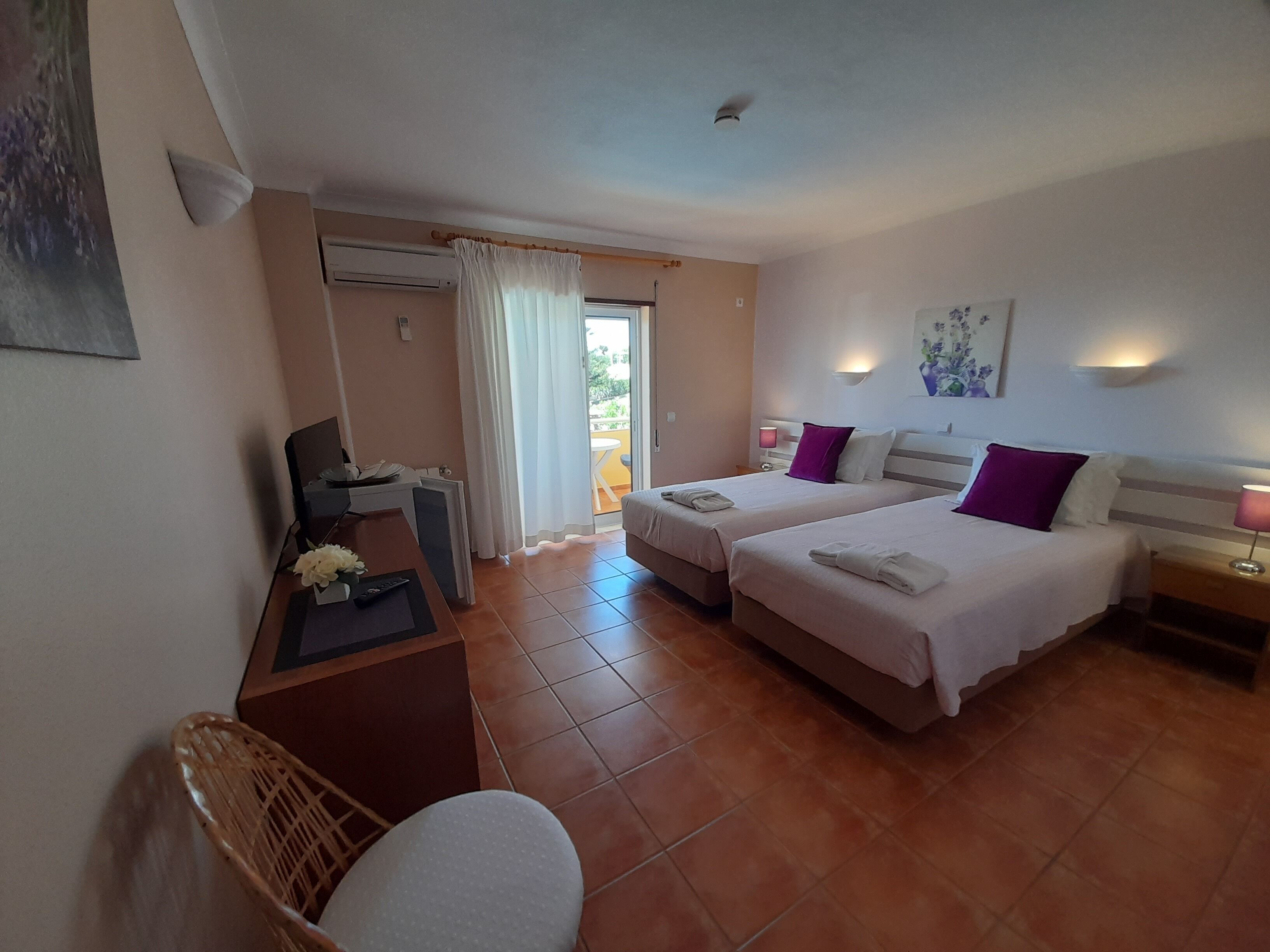 A hotel room with two beds, a desk, a chair, and a balcony.