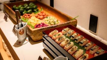 A buffet with various dishes, including sushi, vegetables, and a drink station.