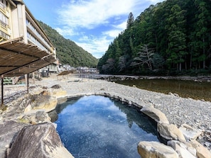 A traditional Japanese onsen with a stone bath surrounded by a rocky landscape and a forested hillside. - Sansuikan Kawayu Midoriya (Tanabe)