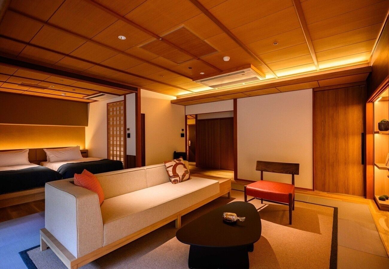 A traditional Japanese-style room with tatami flooring, a low wooden table, a sofa, and a bed with a wooden headboard.