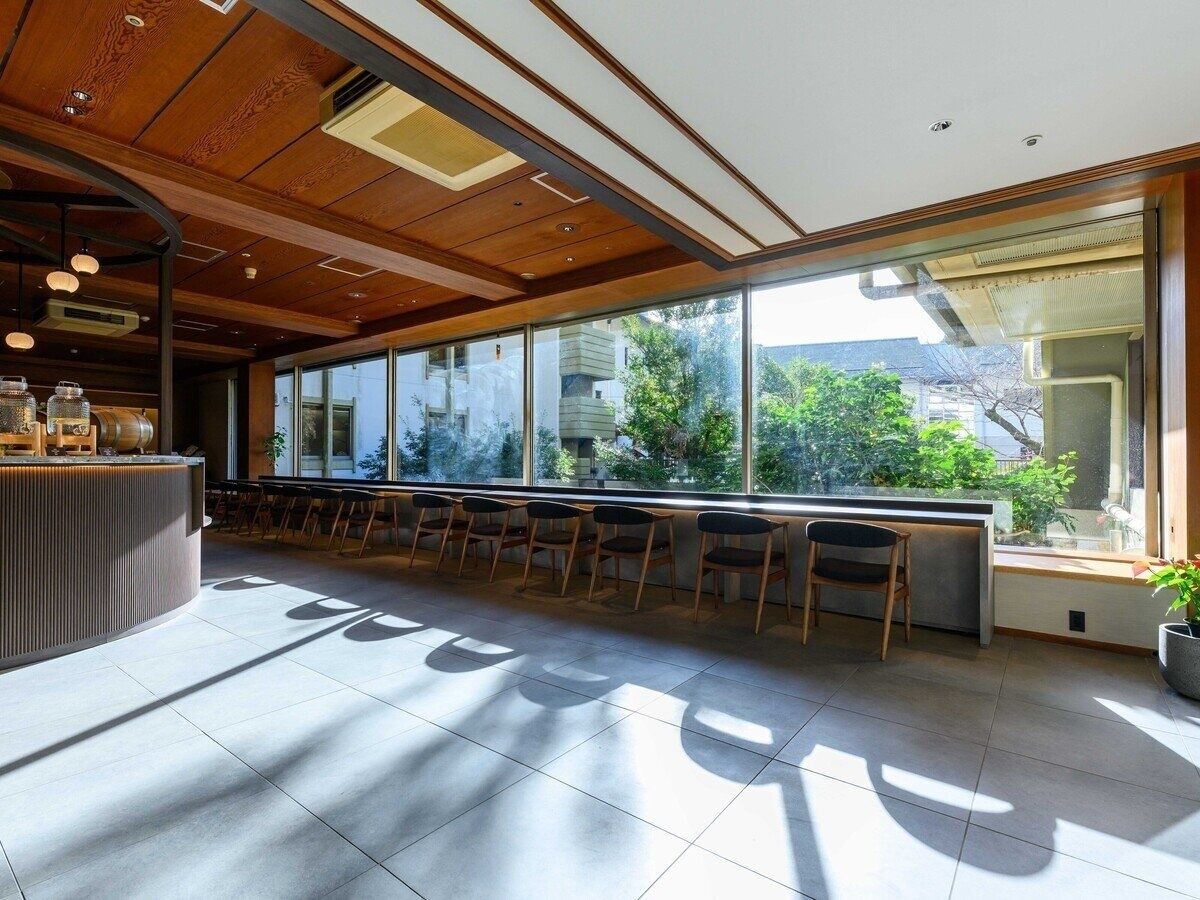 A modern interior with a long counter, seating area, and large windows offering views of greenery and buildings.