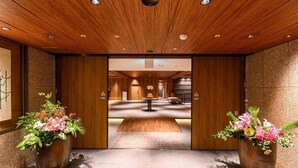 A hotel lobby with wooden paneling, a central reception desk, and two large flower arrangements. - Sansuikan Kawayu Midoriya (Tanabe)