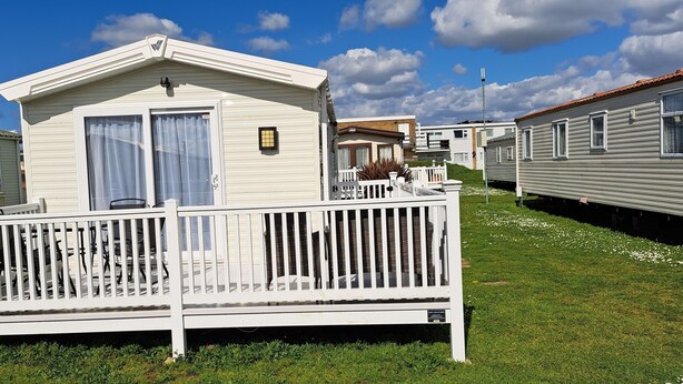 A mobile home with a fenced porch, a small balcony, and a window with curtains. - Beautiful 3-bed Lodge in Kent (New Romney)