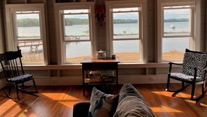 Ein gemütliches Zimmer mit Holzböden, zwei Schaukelstühlen, einer Couch und großen Fenstern mit Blick auf einen See.