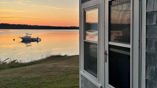 Ein Haus mit Blick auf einen stillen See bei Sonnenuntergang.