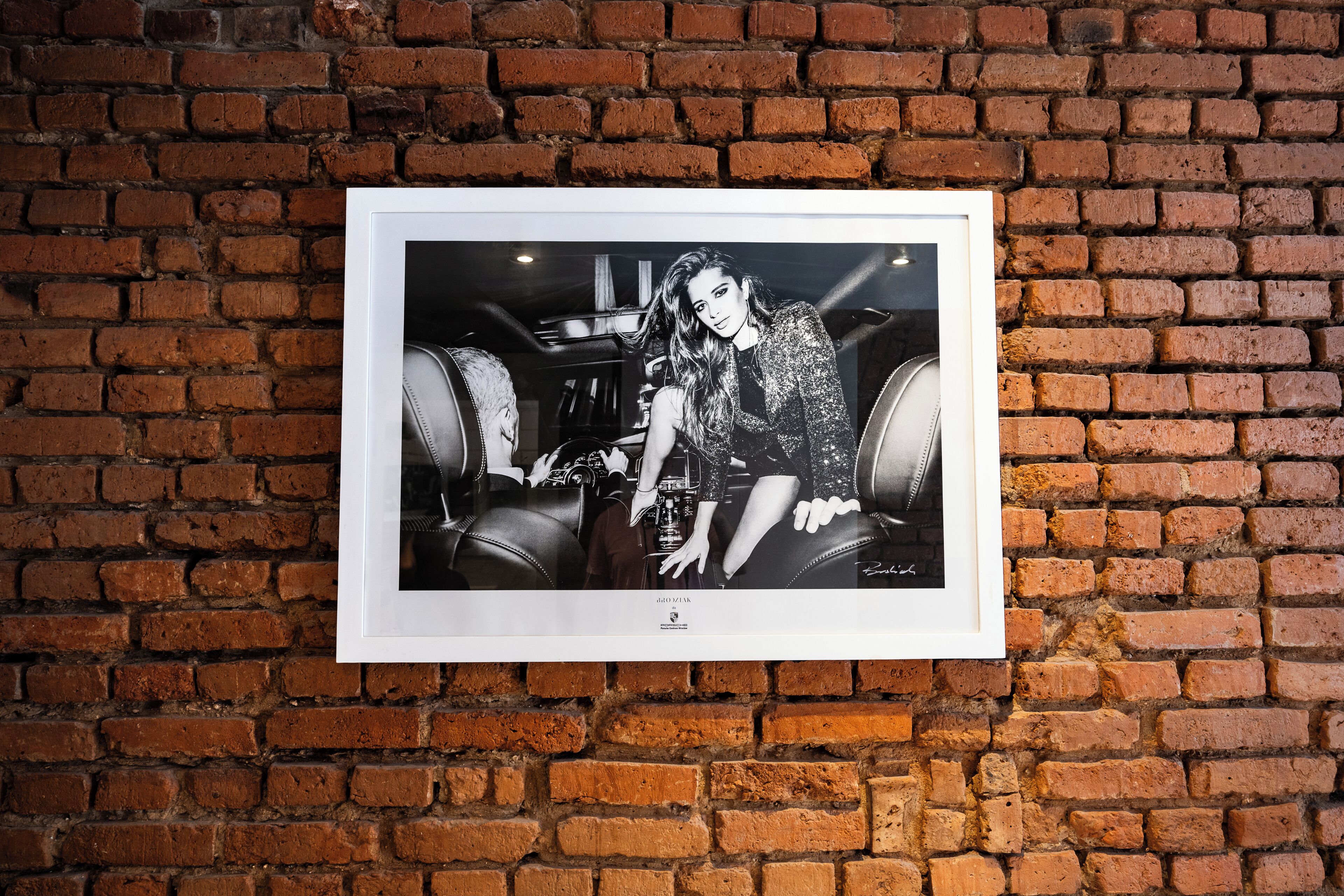 A framed photograph of a person in a room with brick walls and leather furniture.
