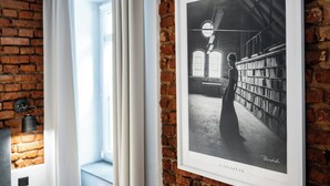 A framed black and white photograph of a library interior with bookshelves and a person in the foreground. - RentPlanet - Apartamenty Rybaki (Poznan)