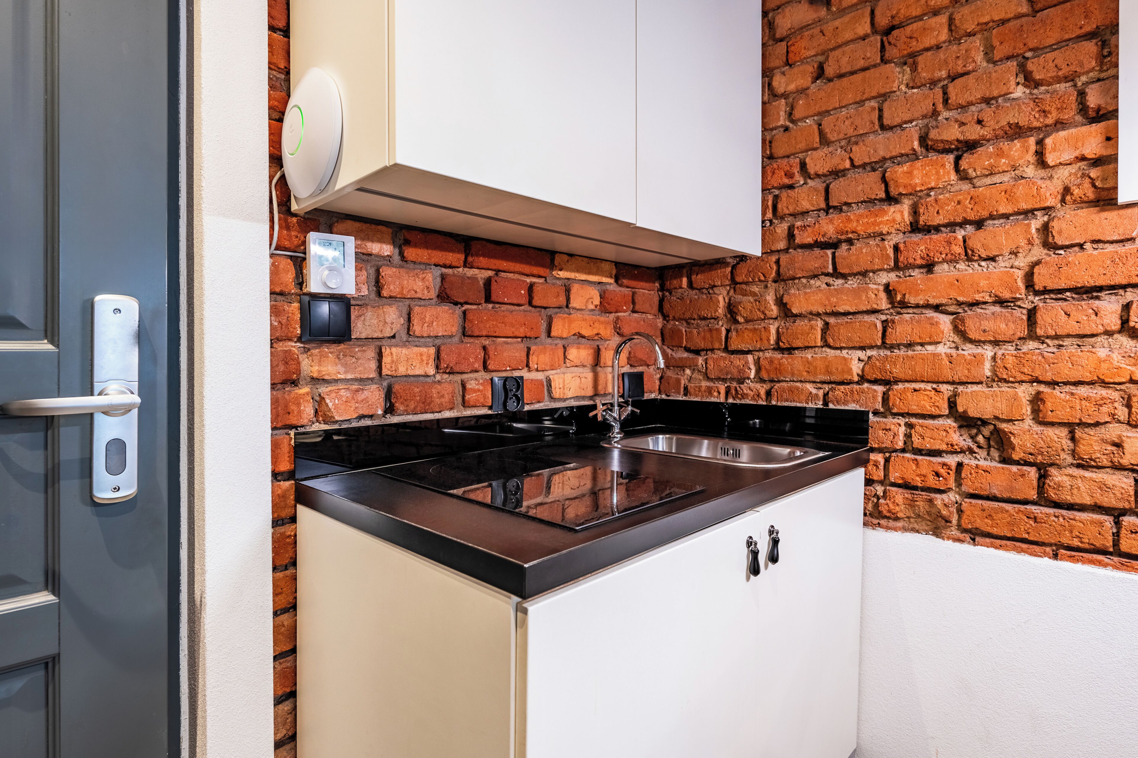 Una cocina compacta con pared de ladrillo, pileta de acero inoxidable y encimera negra.