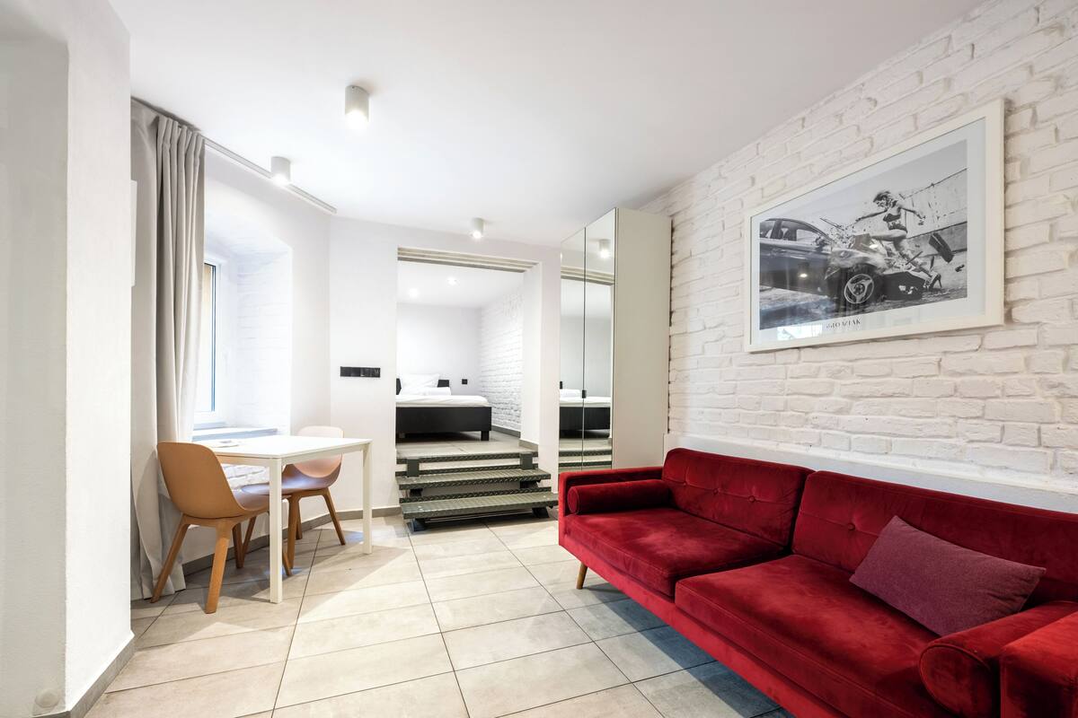 A modern living room with a red sofa, a dining table with chairs, and a staircase leading to a bedroom.