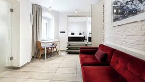 A modern living room with a red sofa, a dining area with a table and chairs, and a bedroom visible through an open door. - RentPlanet - Apartamenty Rybaki (Poznan)