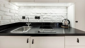 A modern kitchen with a black countertop, white brick backsplash, stainless steel sink, and a kettle. - RentPlanet - Apartamenty Rybaki (Poznan)