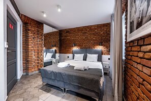 A modern bedroom with a brick wall, a large bed with white bedding, and a small bedside table with a lamp. - RentPlanet - Apartamenty Rybaki (Poznan)