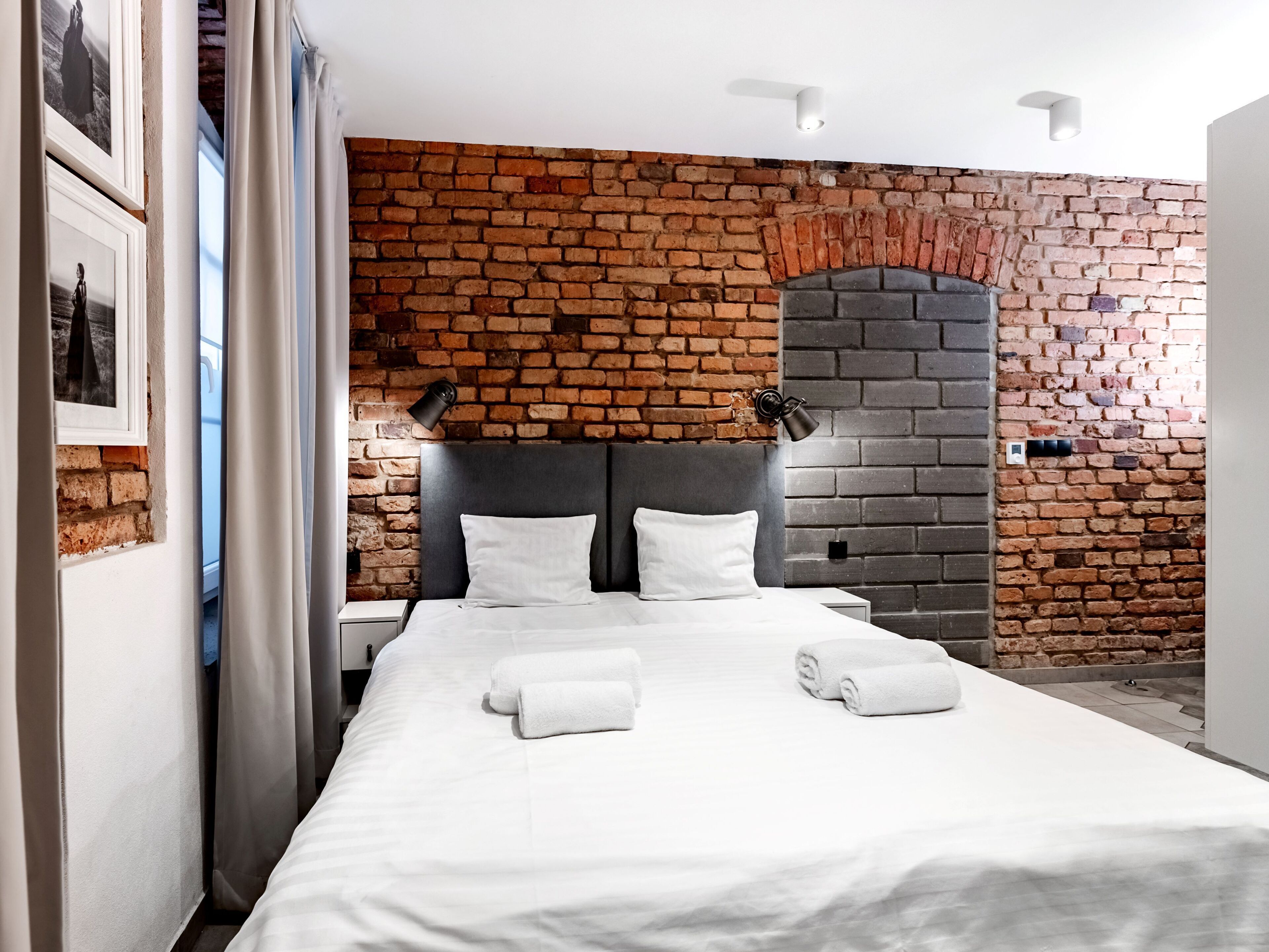 Une chambre d’hôtel avec un mur en briques, un lit recouvert de draps blancs, deux lampes de chevet et une petite cheminée.