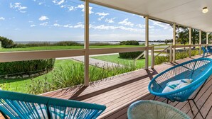 A covered outdoor area with a view of a grassy field and water body. There are blue chairs and a wooden deck. - With stunning views, the Blue House is perfect to relax in affordable Luxury.  (Meningie)