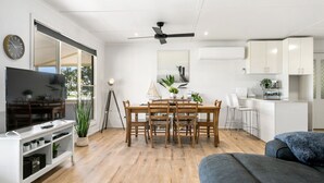 A modern living room with a flat-screen TV, wooden dining table, and a ceiling fan. - With stunning views, the Blue House is perfect to relax in affordable Luxury.  (Meningie)