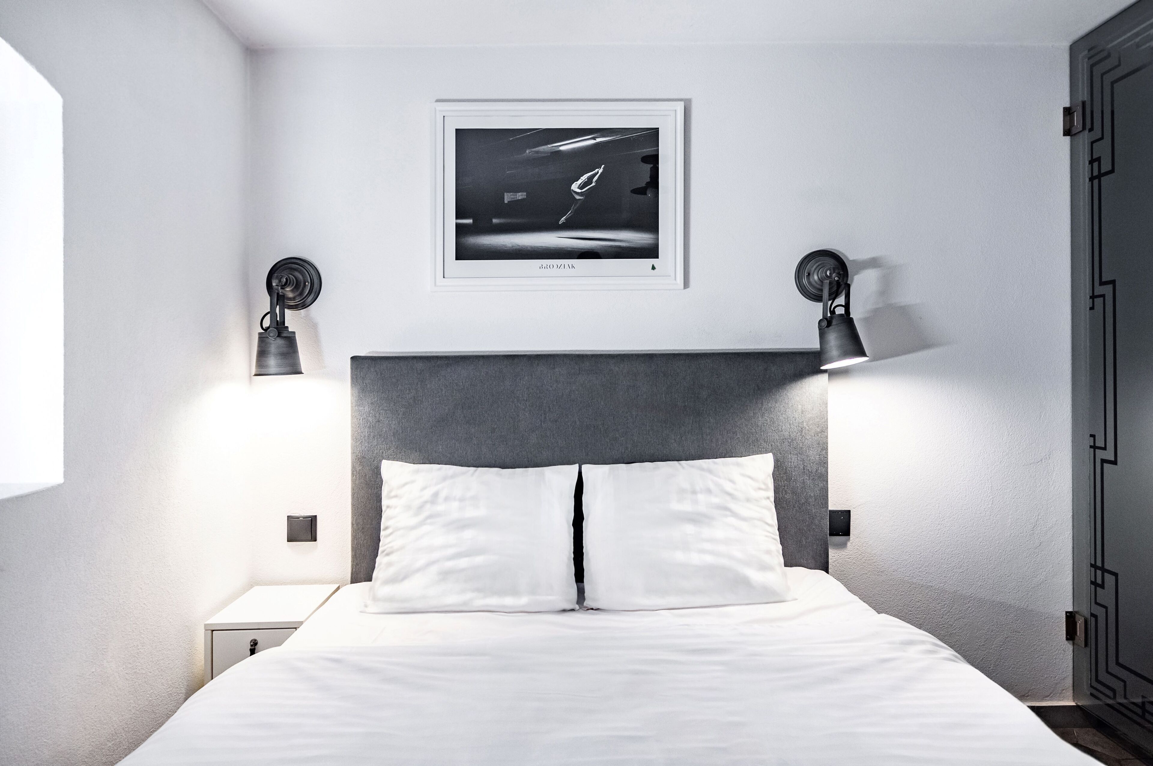 Une chambre d’hôtel moderne avec un grand lit, deux lampes de chevet, un tableau encadré au mur et une table de chevet.