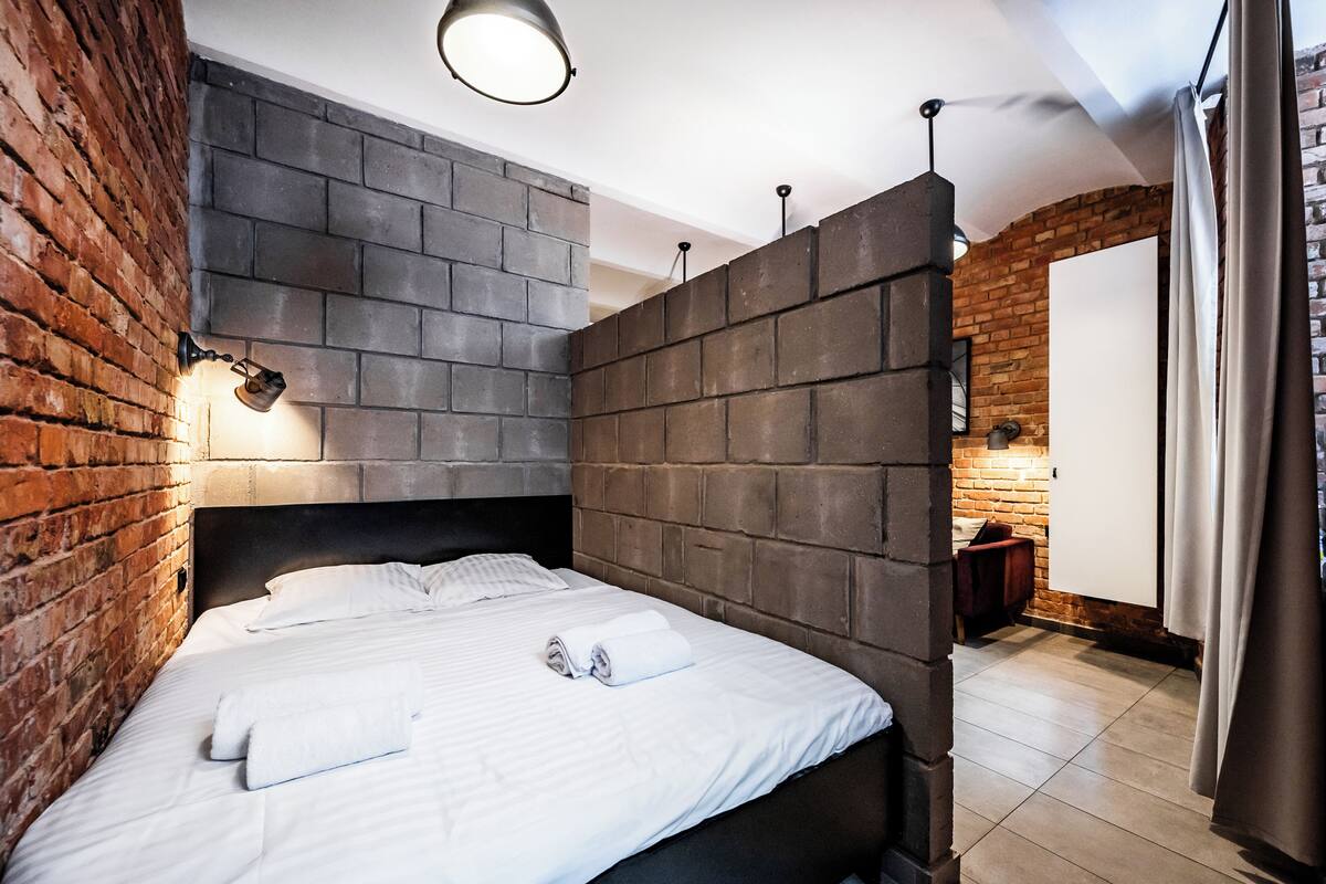 A modern hotel room with a brick accent wall, a neatly made bed, and a small wooden side table.