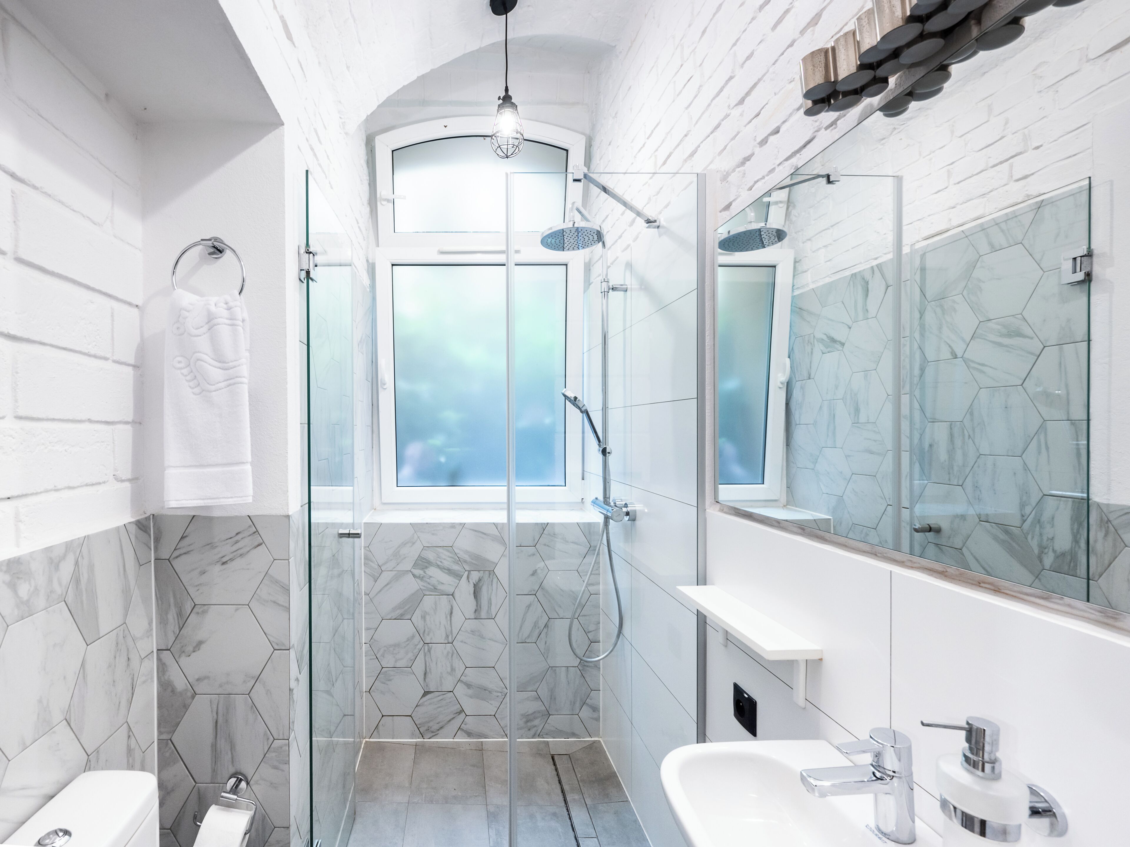 Une salle de bain moderne avec une douche à parois de verre, un grand miroir et un lavabo blanc.