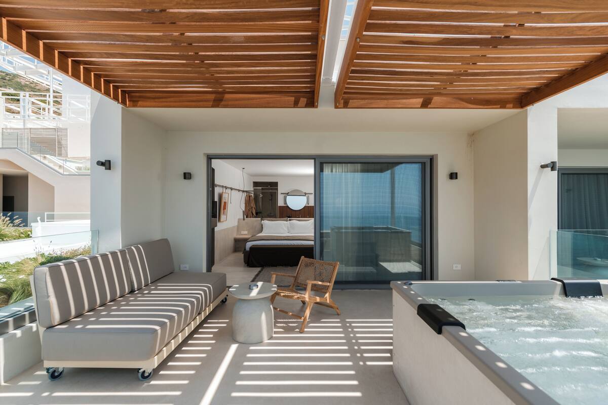 A modern outdoor balcony with a wooden ceiling, a sofa, a chair, a hot tub, and a view of the interior.