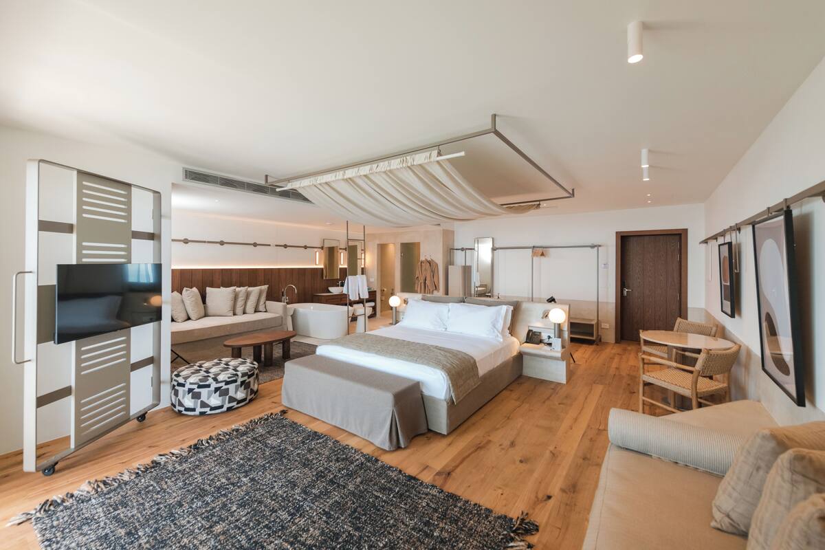 A modern bedroom with a large bed, a sofa, a desk, and a TV.