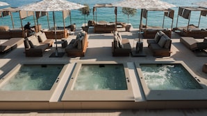 A rooftop pool area with multiple lounge chairs and umbrellas, a hot tub, and a view of the sea. - Folie Marine Beach Hotel & Club (Himare)