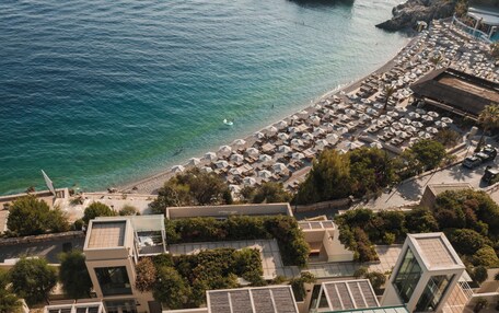 An aerial view of a coastal area with a beach, numerous umbrellas, and buildings.