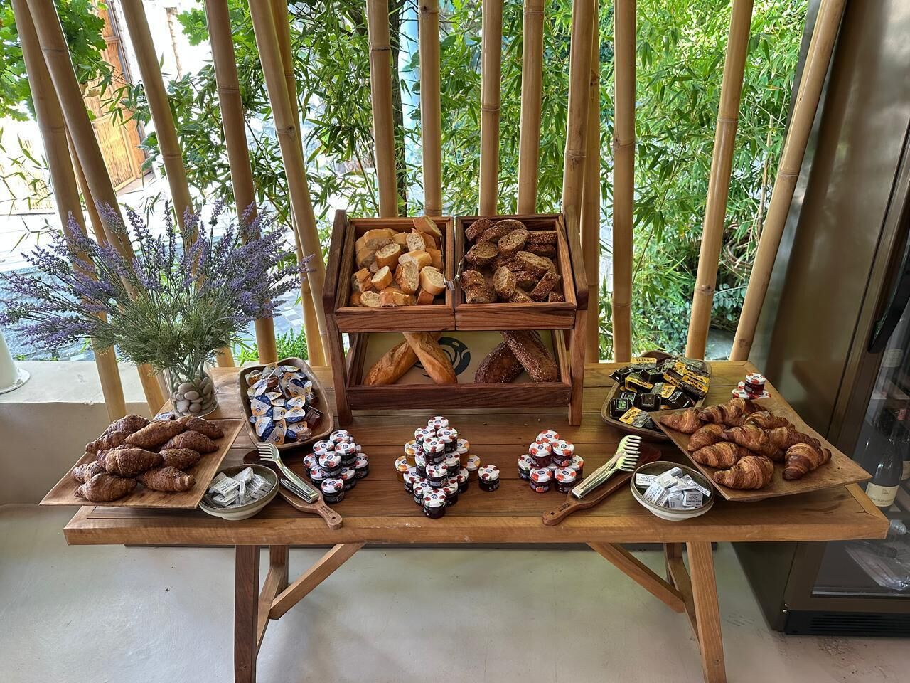 Una mesa de madera con diversos alimentos y condimentos, con un fondo de bambú y follaje.