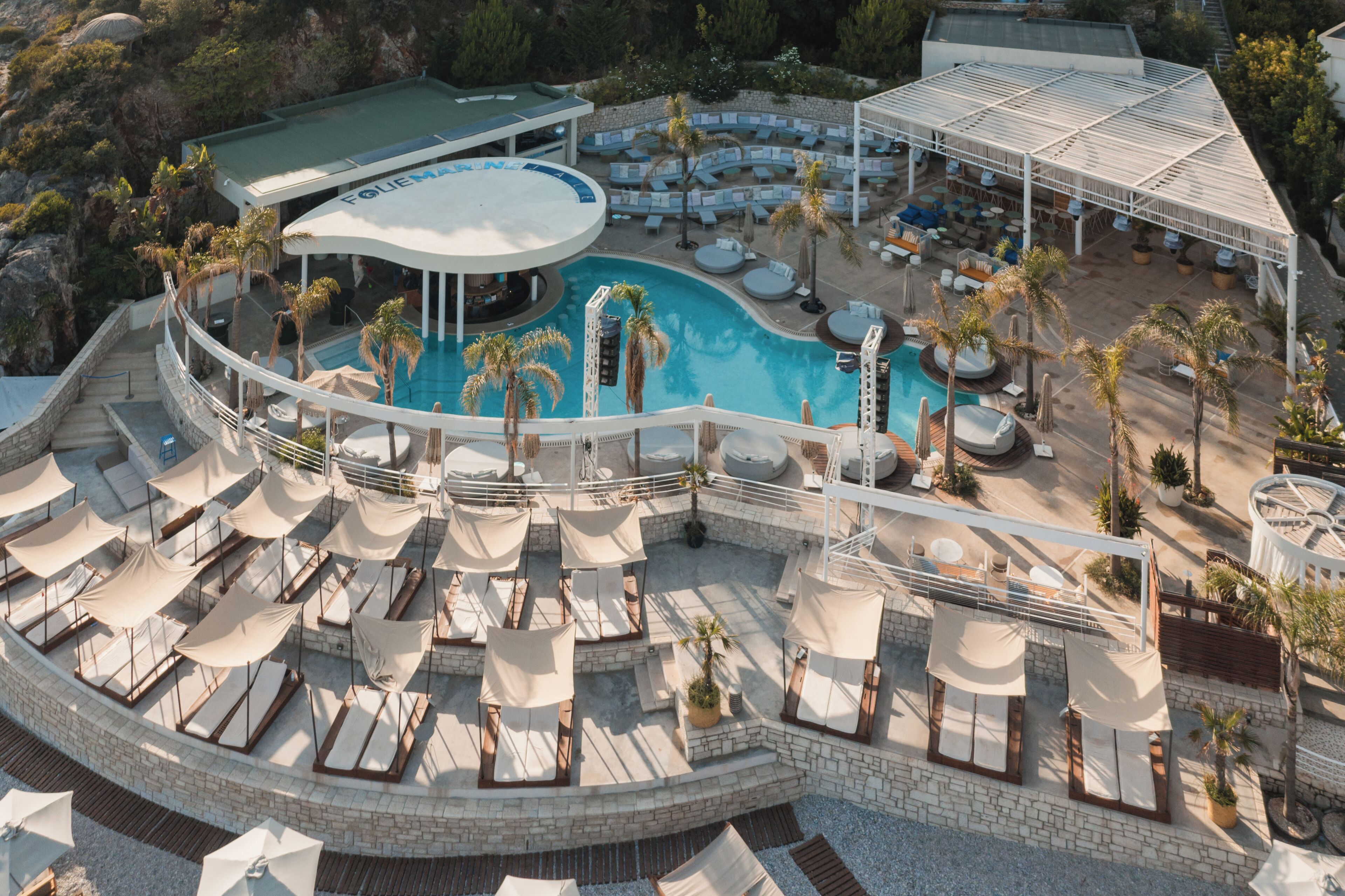 An aerial view of a resort with a large pool, sun loungers, and a covered seating area.