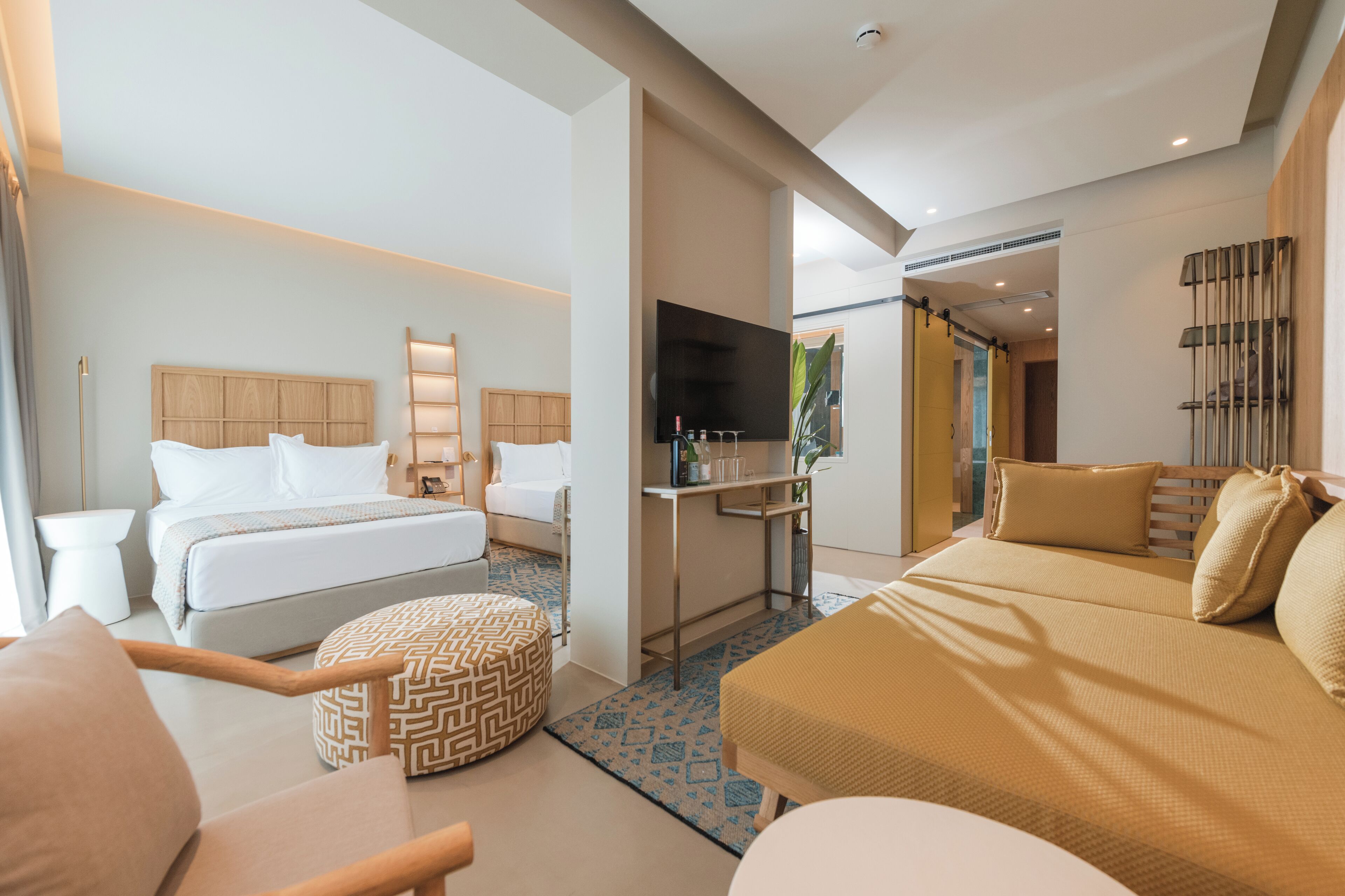 A modern hotel room with a bed, a sofa, a desk, and a TV.