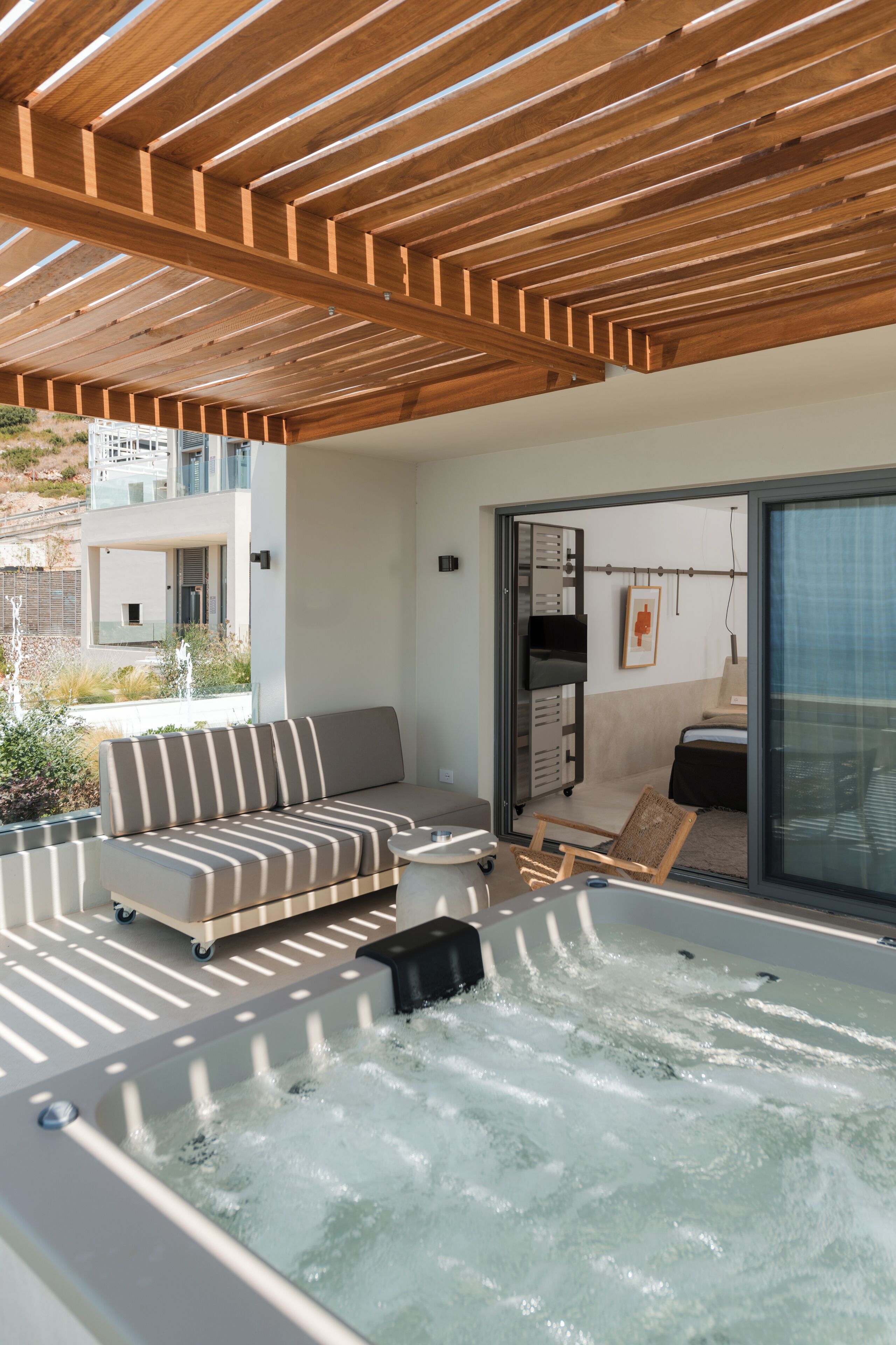 Un área moderna de hidromasaje al aire libre con techo de madera, un sofá, una silla y una puerta corrediza de vidrio que da a un balcón.
