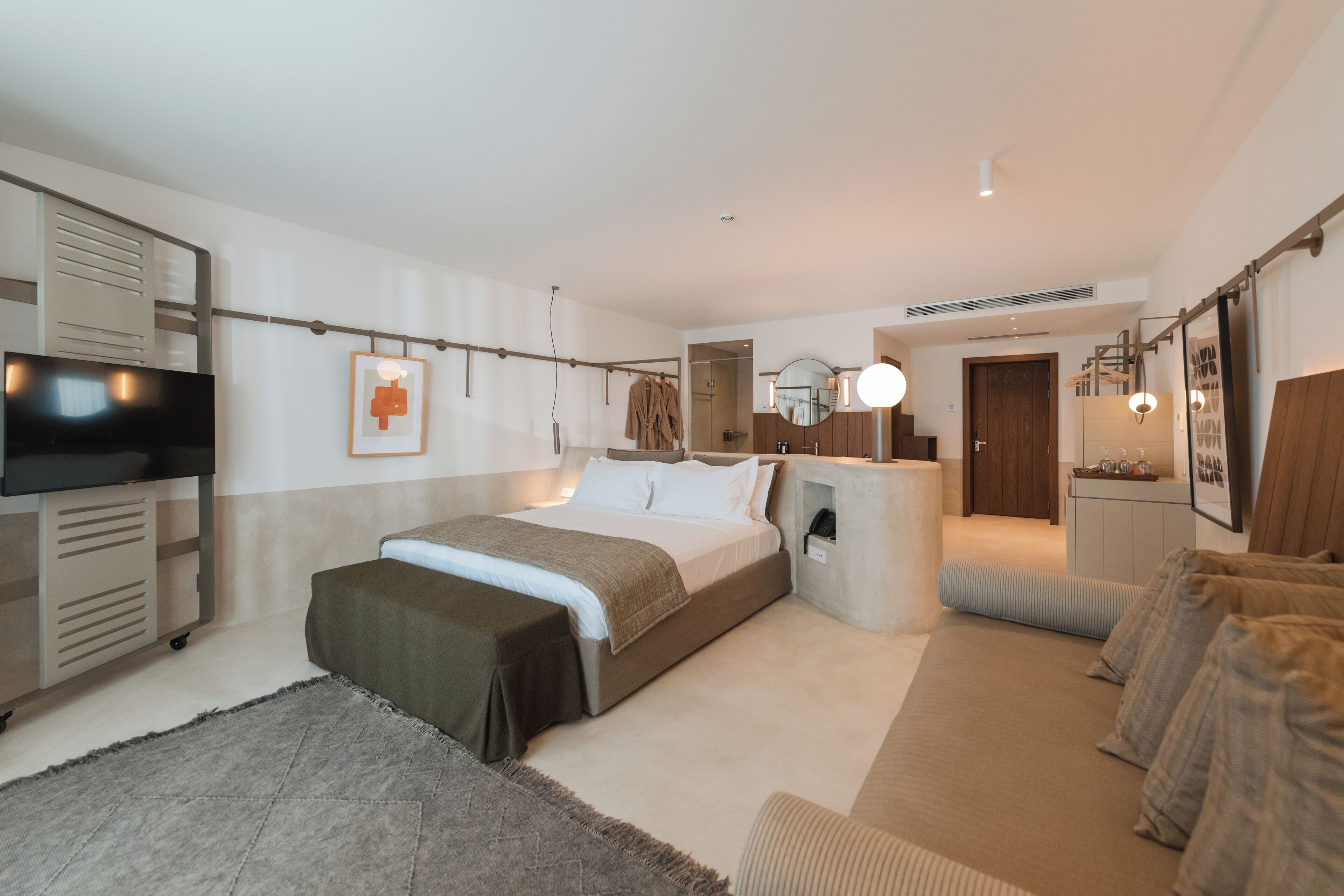 Ein modernes Hotelzimmer mit einem großen Bett, einer Sitzecke, einem Fernseher und einem Kleiderschrank.