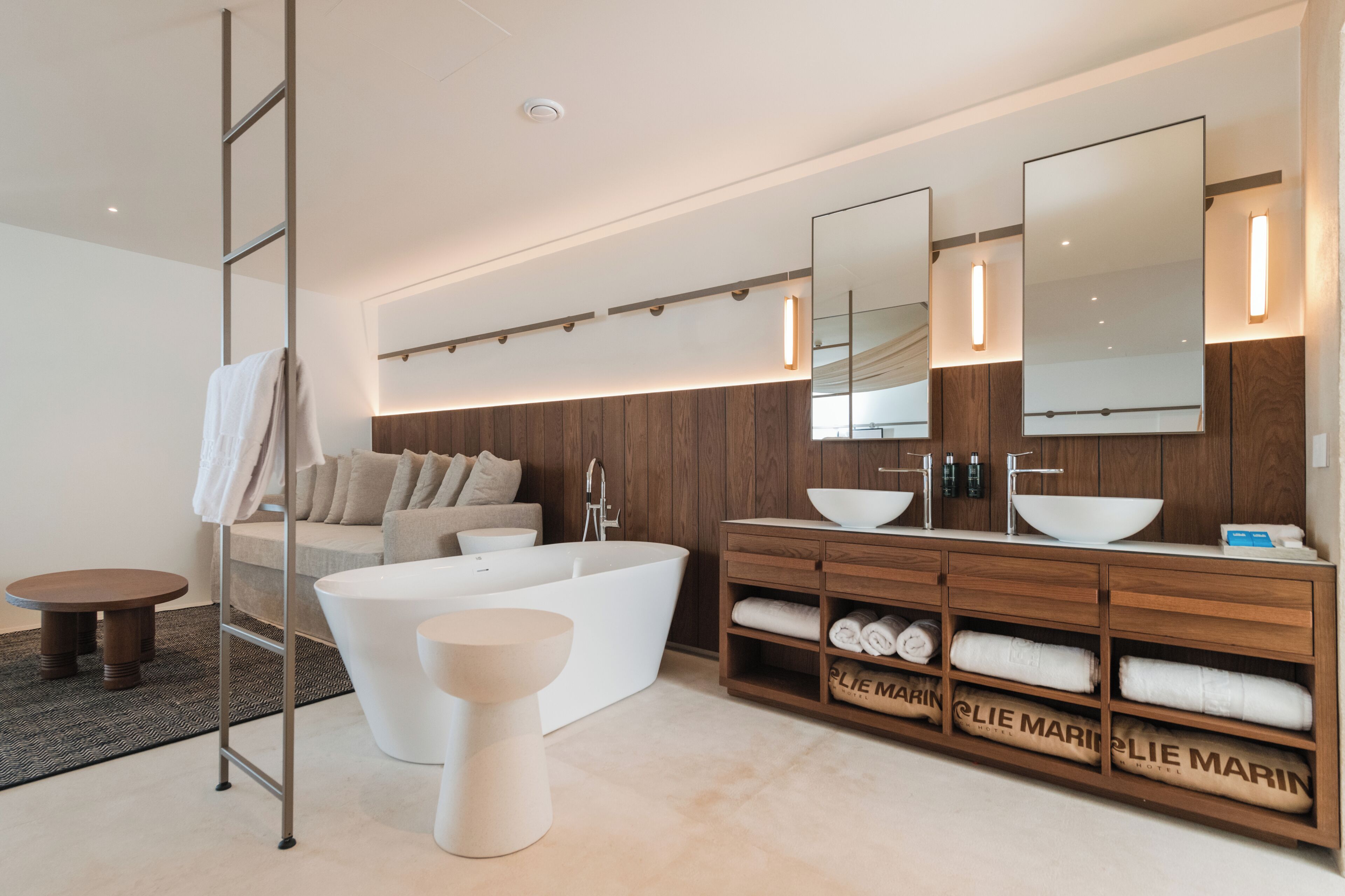 A modern bathroom with a freestanding bathtub, a vanity with a large mirror, and a wooden vanity with towels.