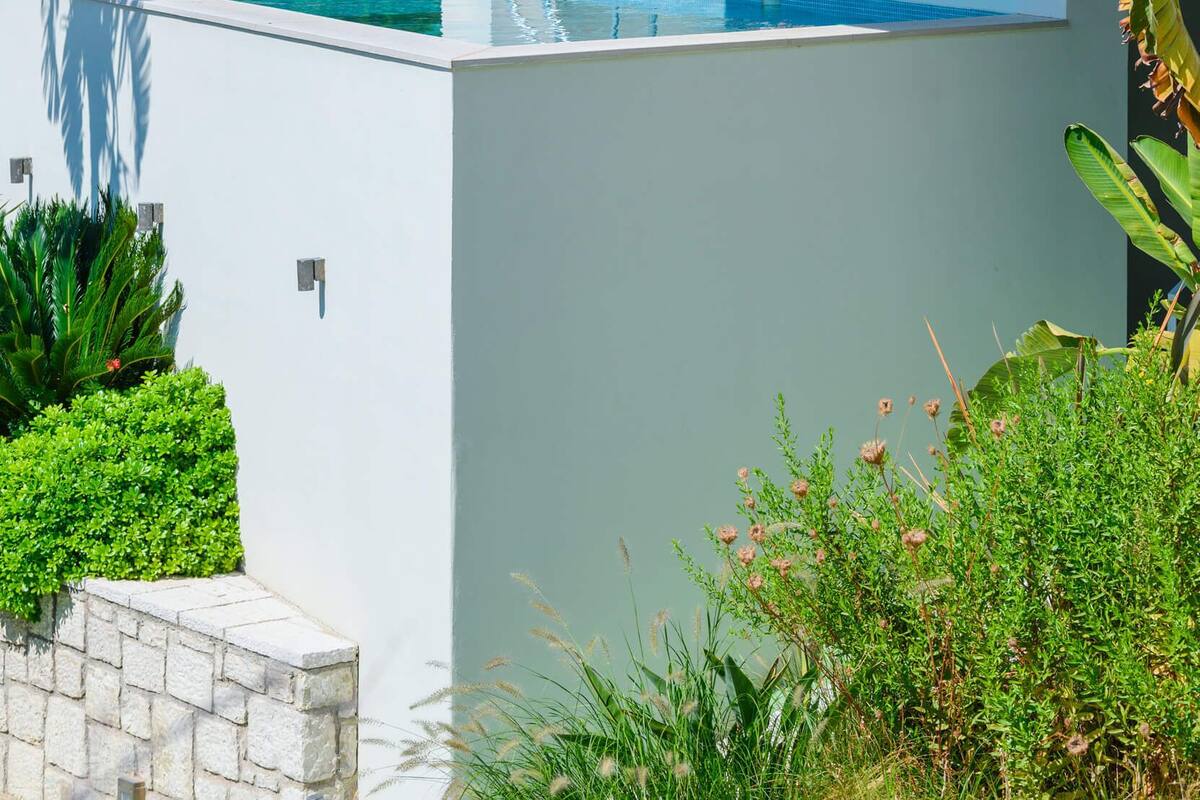A modern outdoor pool area with a wooden deck, a built-in seating area, and lush greenery surrounding the space.