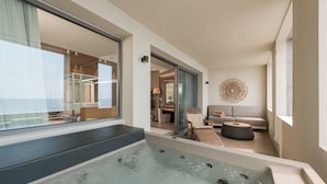 A modern bathroom with a large bathtub, a glass shower enclosure, and a view of the living area with a sofa and a decorative wall piece. - Folie Marine Beach Hotel & Club (Himare)