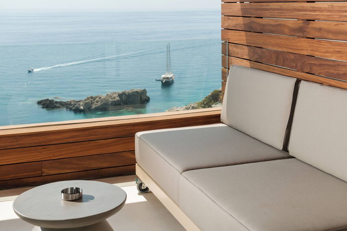 A modern outdoor seating area with a view of the sea and a sailboat.