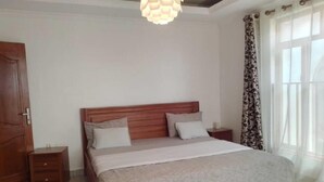 A bedroom with a wooden bed, a nightstand, a small rug, and a hanging light fixture. - ibizza resort (Shingiro)
