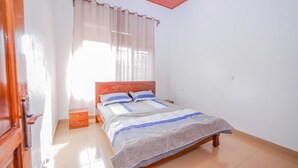A bedroom with a wooden bed, white curtains, a nightstand, and a tiled floor. - ibizza resort (Shingiro)
