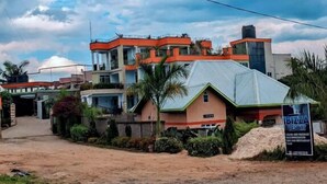 A multi-story building with a prominent orange and white color scheme, a signboard for a restaurant, and a dirt road in front. - ibizza resort (Shingiro)