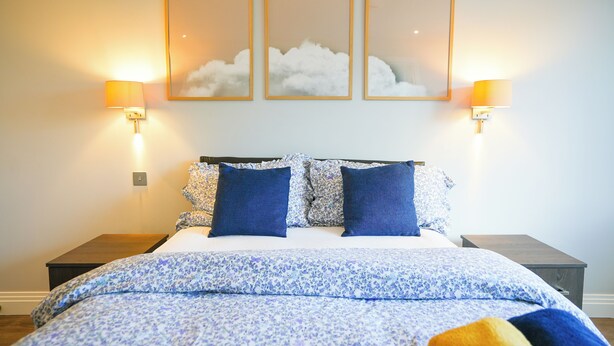 A bedroom with a bed, two nightstands, and three wall-mounted lamps.