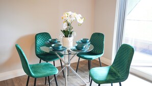 A dining area with a glass table surrounded by teal chairs, a vase with white flowers, and teal dinnerware.