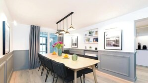 Een moderne keuken met een eethoek, met hanglampen, een lange tafel en een uitzicht op de stad door grote ramen.