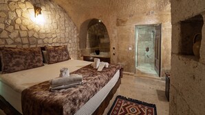 Dormitorio de paredes de piedra con cama, toallas, ducha y alfombra.