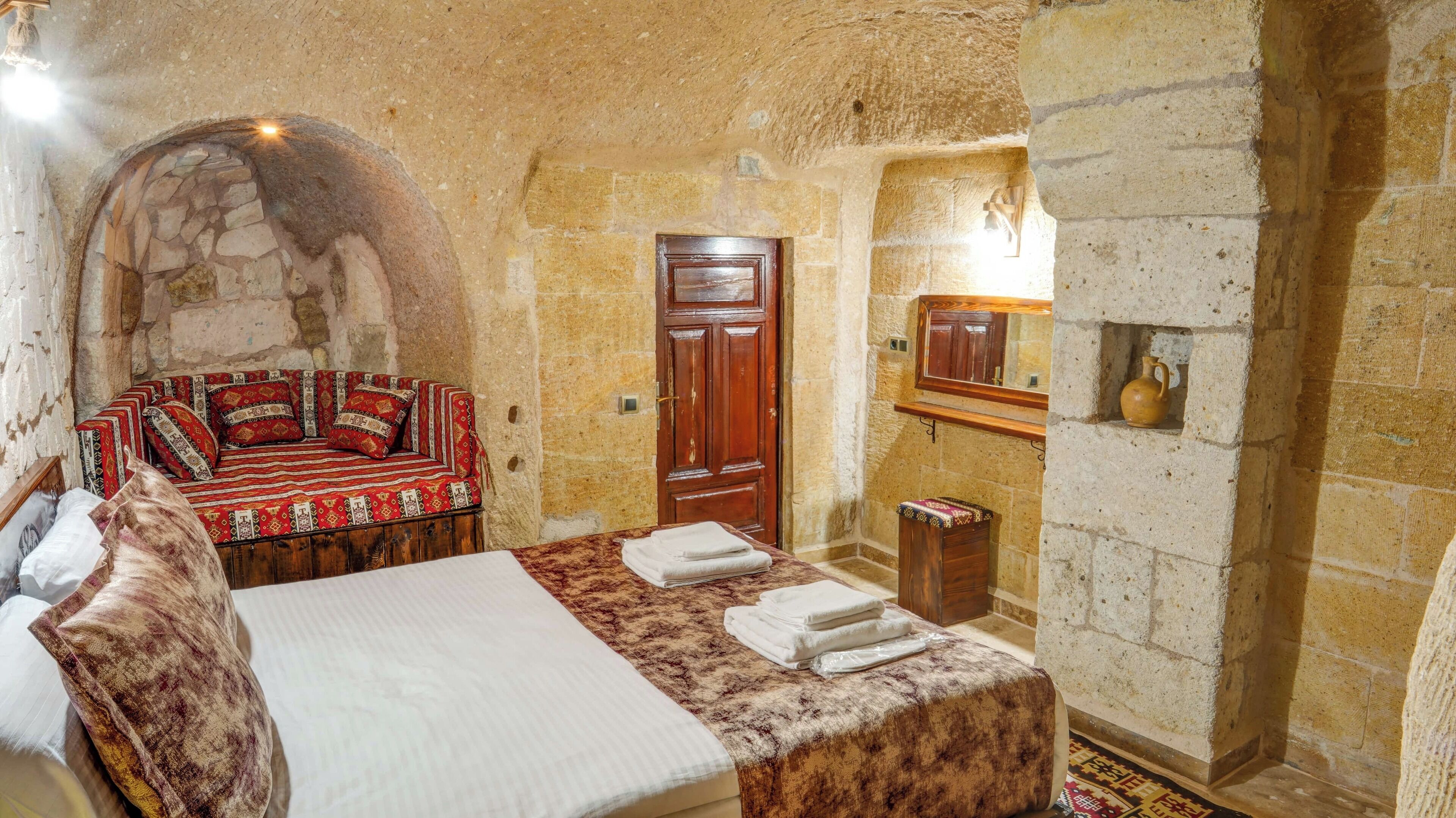 A traditional stone-walled room with a bed, a wooden door, and a small wooden cabinet.